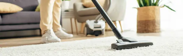 Um homem bonito em roupa de casa aconchegante aspirando um tapete. — Fotografia de Stock
