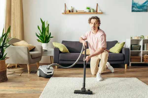 A handsome man in cozy homewear diligently vacuuming a living room. — Stock Photo