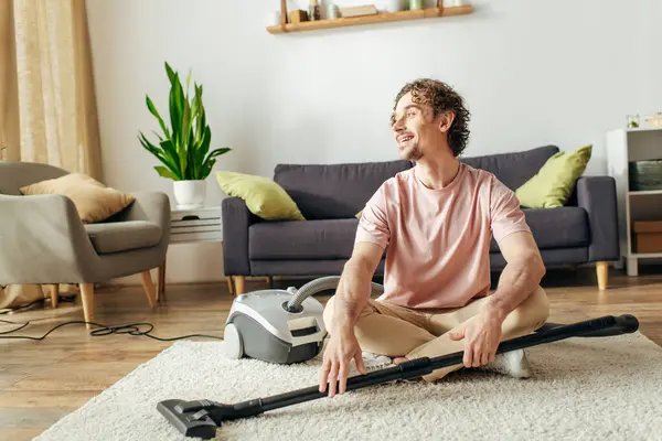 A handsome man in cozy homewear sits in front of a vacuum cleaner. — Stock Photo