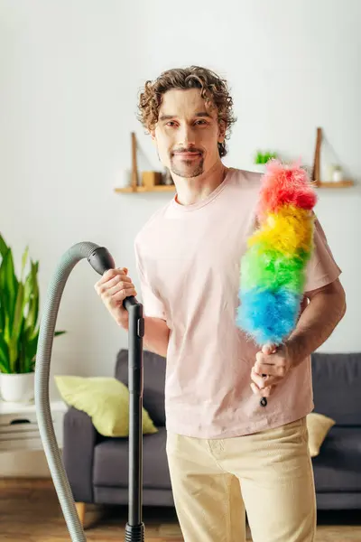 Handsome man in cozy homewear holding a colorful toy while vacuuming. — Stock Photo