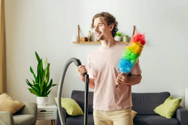 A stylish man holding a colorful toy next to a vacuum cleaner in a cozy home. — Stock Photo