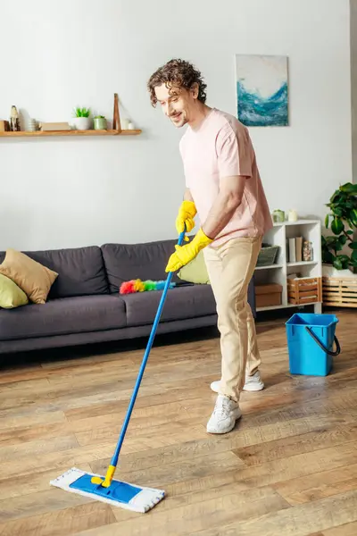 A handsome man in cozy homewear diligently mops the floor. — Stock Photo