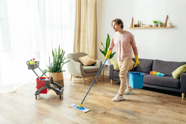 Ein Mann in kuscheliger Hauskleidung putzt sein Wohnzimmer mit einem Wischmopp. — Stockfoto