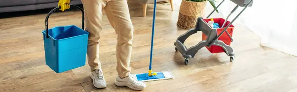 Un uomo in accogliente biancheria da casa pulisce il pavimento diligentemente. — Foto stock