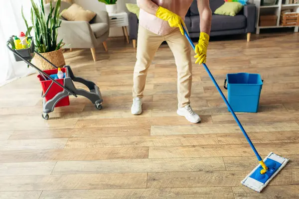 A handsome man in cozy homewear cleans the floor with a mop. — Stock Photo