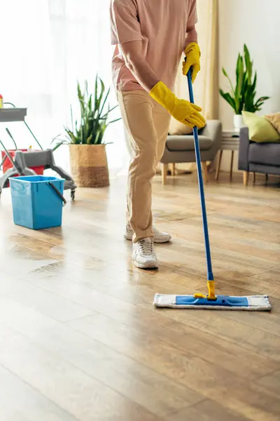 A handsome man in cozy homewear mops the floor. — Stock Photo