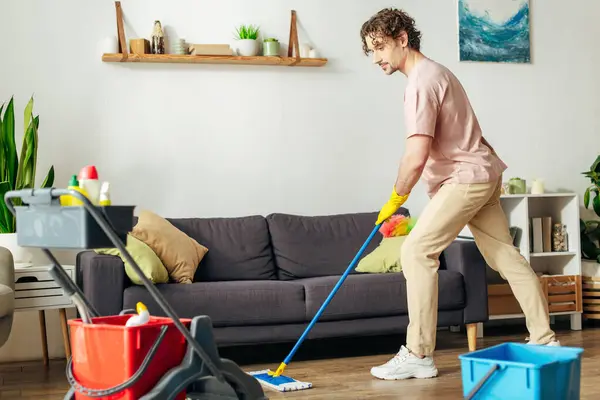 Un bell'uomo in casalinghi accoglienti pulisce meticolosamente un soggiorno con uno straccio. — Foto stock