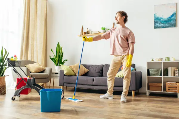 A handsome man in cozy homewear cleaning the living room with a mop and bucket. — Stock Photo