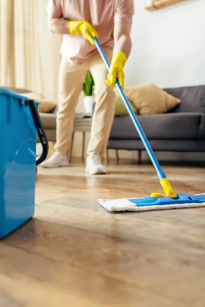 Un bell'uomo in casalinghe accoglienti pulisce diligentemente il pavimento. — Foto stock