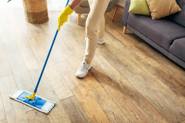 Ein gutaussehender Mann in gemütlicher Hauskleidung putzt mit einem Wischmopp einen Holzboden. — Stockfoto