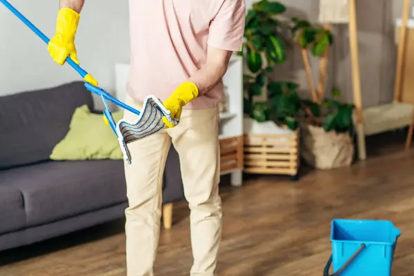 A man in cozy homewear expertly cleans the living room with a mop. — Stock Photo