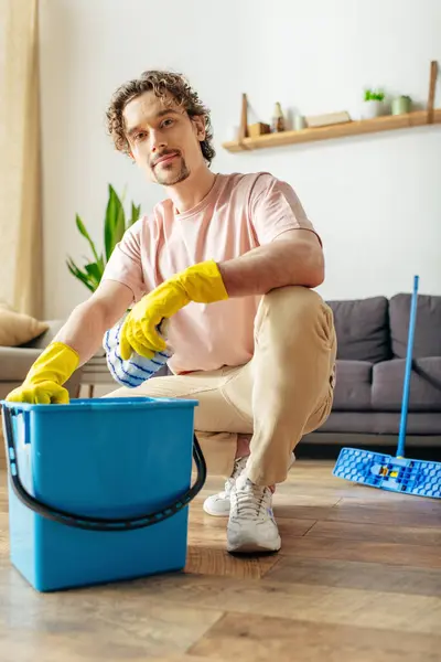 A handsome man in cozy homewear cleaning the floor with a bucket. — Stock Photo