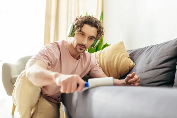 Handsome man in cozy homewear sitting on couch with sticky roller in hand. — Stock Photo