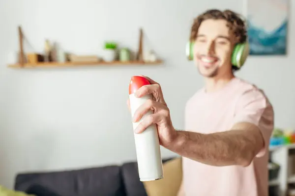 Ein Mann in kuscheliger Homewear hält ein Spray in der Hand, während er Kopfhörer trägt, vertieft in musikalische Harmonie. — Stockfoto
