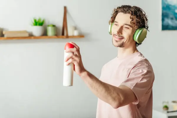 Young man in headphones holds spray bottle while cleaning. — Stock Photo