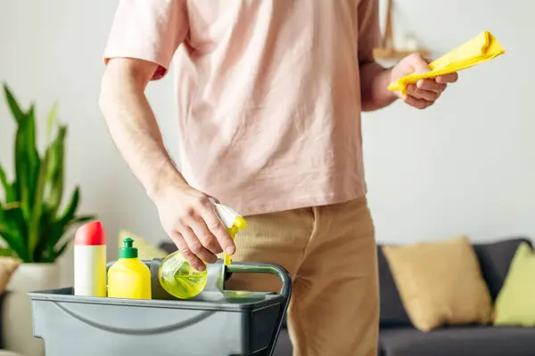 A man in cozy homewear cleans a living room with a yellow sprays. — Stock Photo