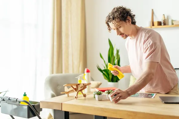 Handsome man in cozy homewear cleaning at table with yellow spray in hand. — Stock Photo