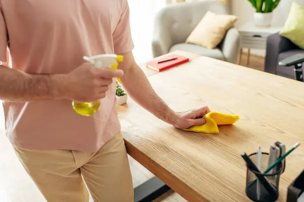 Bello uomo in accogliente biancheria da casa pulizia di un tavolo con un panno giallo. — Foto stock