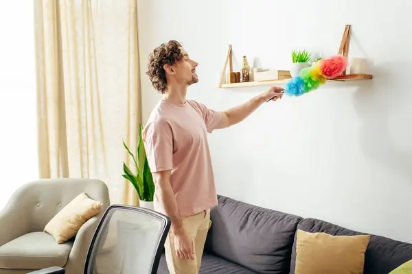 A handsome man in cozy homewear cleaning a living room with a duster. — Stock Photo