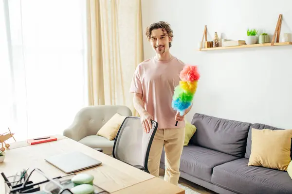 Bonito homem em homewear acolhedor segurando um espanador vibrante na sala de estar elegante. — Fotografia de Stock