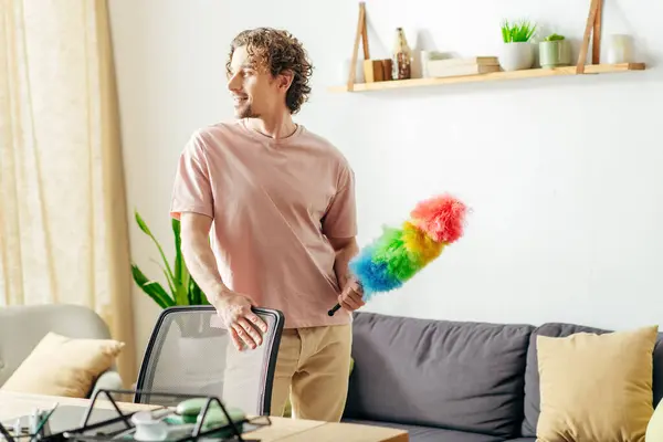 Um homem elegante limpa a sala com um espanador. — Fotografia de Stock