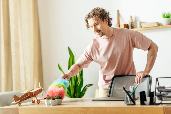 Stylish man in pink shirt cleaning home with duster indoors. — Stock Photo