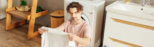 Ein gutaussehender Mann in gemütlicher Homewear steht neben einer Waschmaschine im Badezimmer. — Stockfoto