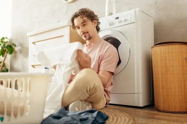 Um homem de roupa de casa aconchegante senta-se ao lado de uma máquina de lavar roupa em uma farra de limpeza. — Fotografia de Stock