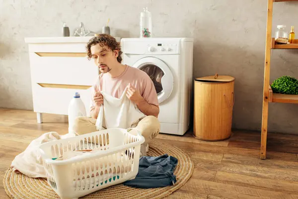 A handsome man in cozy homewear sitting next to a washing machine. — Stock Photo