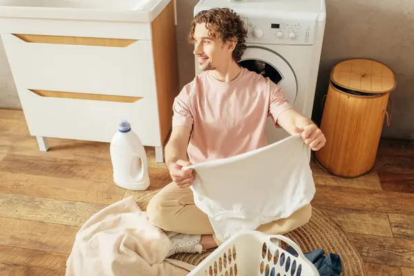 Un bel homme dans des vêtements confortables assis à côté d'une machine à laver. — Photo de stock