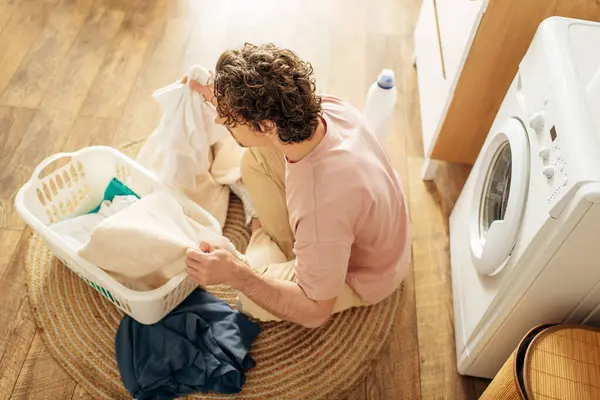 Um homem de roupa de casa aconchegante sentado ao lado de uma máquina de lavar roupa. — Fotografia de Stock