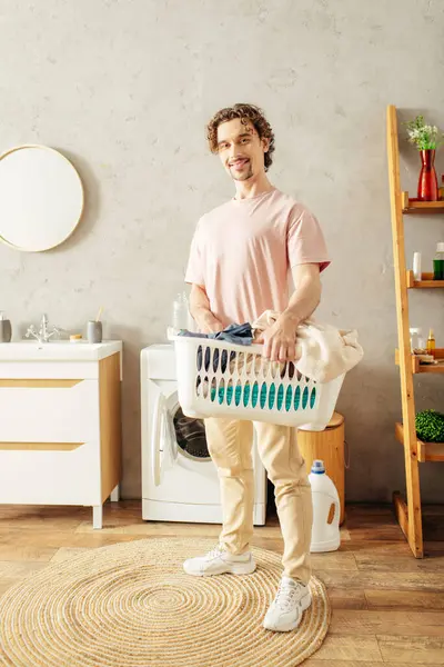 Ein gutaussehender Mann in gemütlicher Hauskleidung hält einen Wäschekorb in einem Raum. — Stockfoto