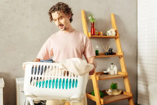 Um homem bonito em roupa de casa aconchegante segurando uma cesta de lavanderia em um banheiro. — Fotografia de Stock