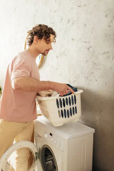 Ein Mann in kuscheliger Hauskleidung lädt einen Wäschekorb auf eine Waschmaschine. — Stockfoto