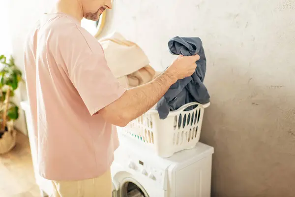 Um homem bonito em roupa de casa aconchegante fica ao lado de uma máquina de lavar roupa. — Fotografia de Stock