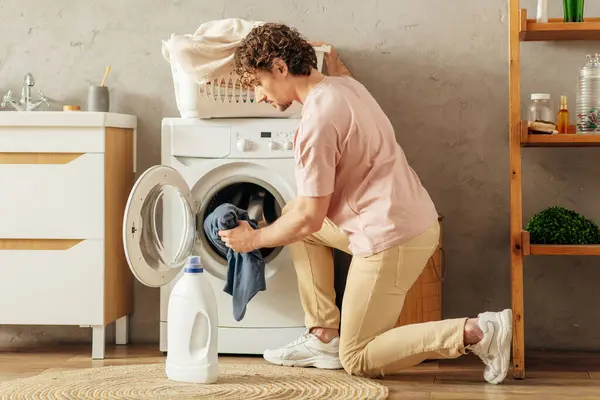 Homem carrega alegremente roupas na máquina de lavar roupa. — Fotografia de Stock