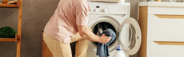 Ein Mann legt Kleidung vorsichtig in eine Waschmaschine. — Stockfoto