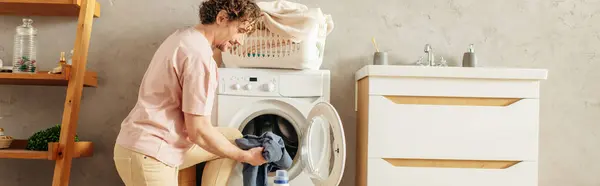 Мужчина аккуратно загружает одежду в стиральную машину. — стоковое фото
