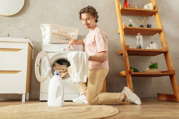 A man in cozy homewear sits in front of a washing machine. — Stock Photo