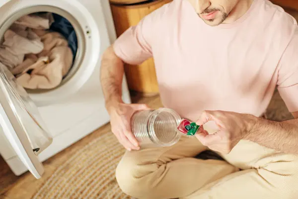 Um homem de roupa de casa confortável senta-se no chão, segurando um detergente. — Fotografia de Stock