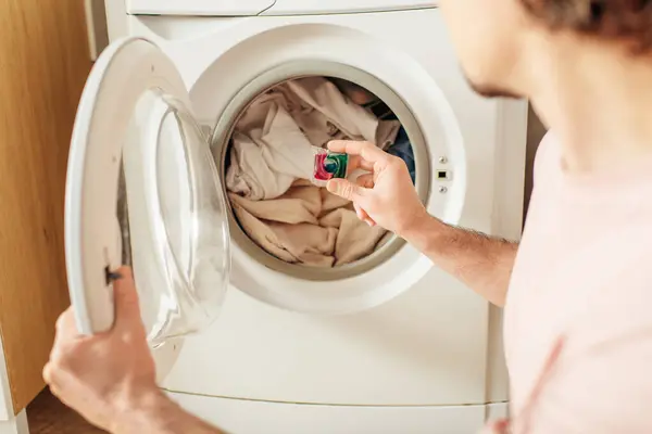 Ein gutaussehender Mann in gemütlicher Hauskleidung, der Waschmittel in die Waschmaschine gibt. — Stockfoto