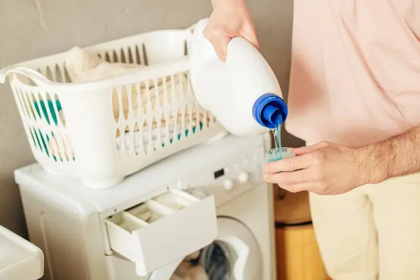 Schöner Mann in kuscheliger Homewear gießt Waschmittel in Waschmaschine. — Stockfoto