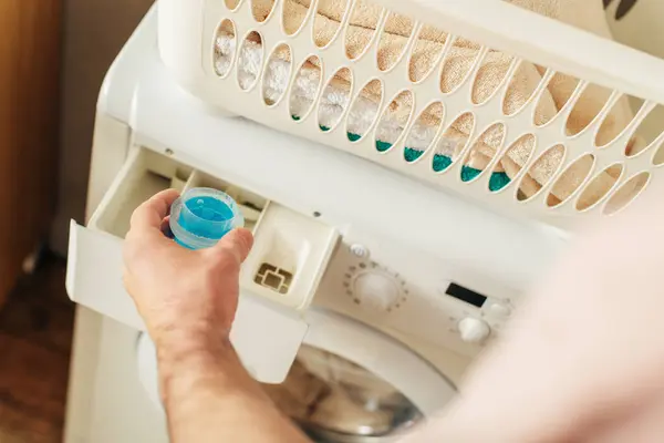 Schöner Mann in kuscheliger Homewear lädt Waschmittel in die Waschmaschine. — Stockfoto