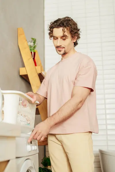 Um homem bonito em roupa de casa aconchegante em frente a uma máquina de lavar roupa. — Fotografia de Stock