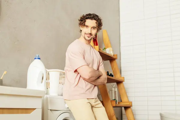A handsome man in cozy homewear standing next to a washing machine, ready for laundry day. — Stock Photo