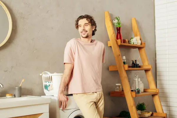 Schöner Mann in gemütlicher Homewear, der neben einer Waschmaschine im Badezimmer steht. — Stockfoto