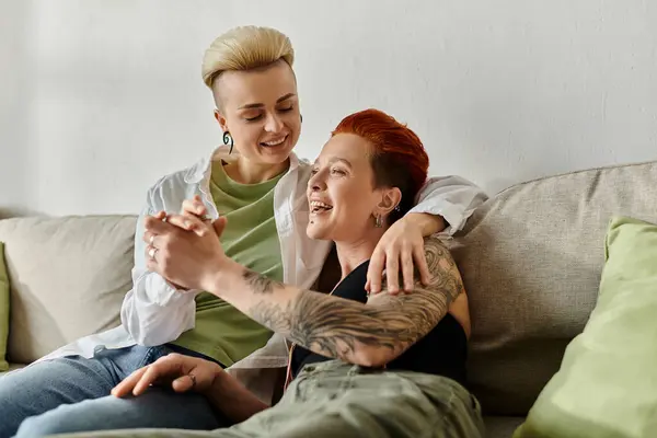 Due donne, una coppia lesbica, con capelli corti e tatuaggi, si rilassano insieme su un divano. — Foto stock