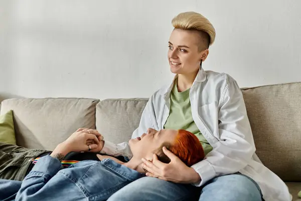 Una coppia lesbica con i capelli corti seduta da vicino su un divano, che condivide un tenero momento di intimità a casa. — Stock Photo