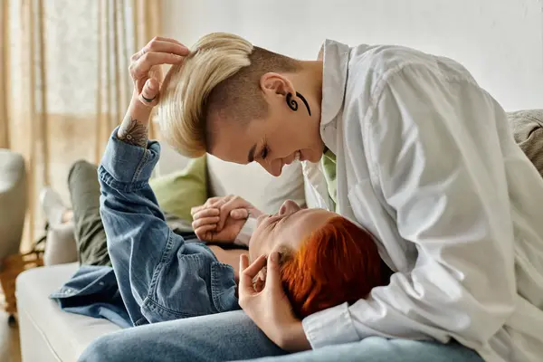 Two women with short hair sit on a cozy couch, wrapped in a loving hug, showcasing the beauty of connection. — Stock Photo