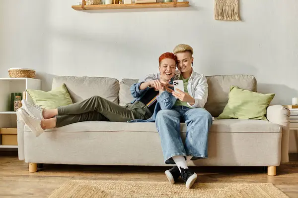 Due donne, una coppia lesbica con i capelli corti, si siedono insieme su un divano nella loro accogliente casa. — Foto stock